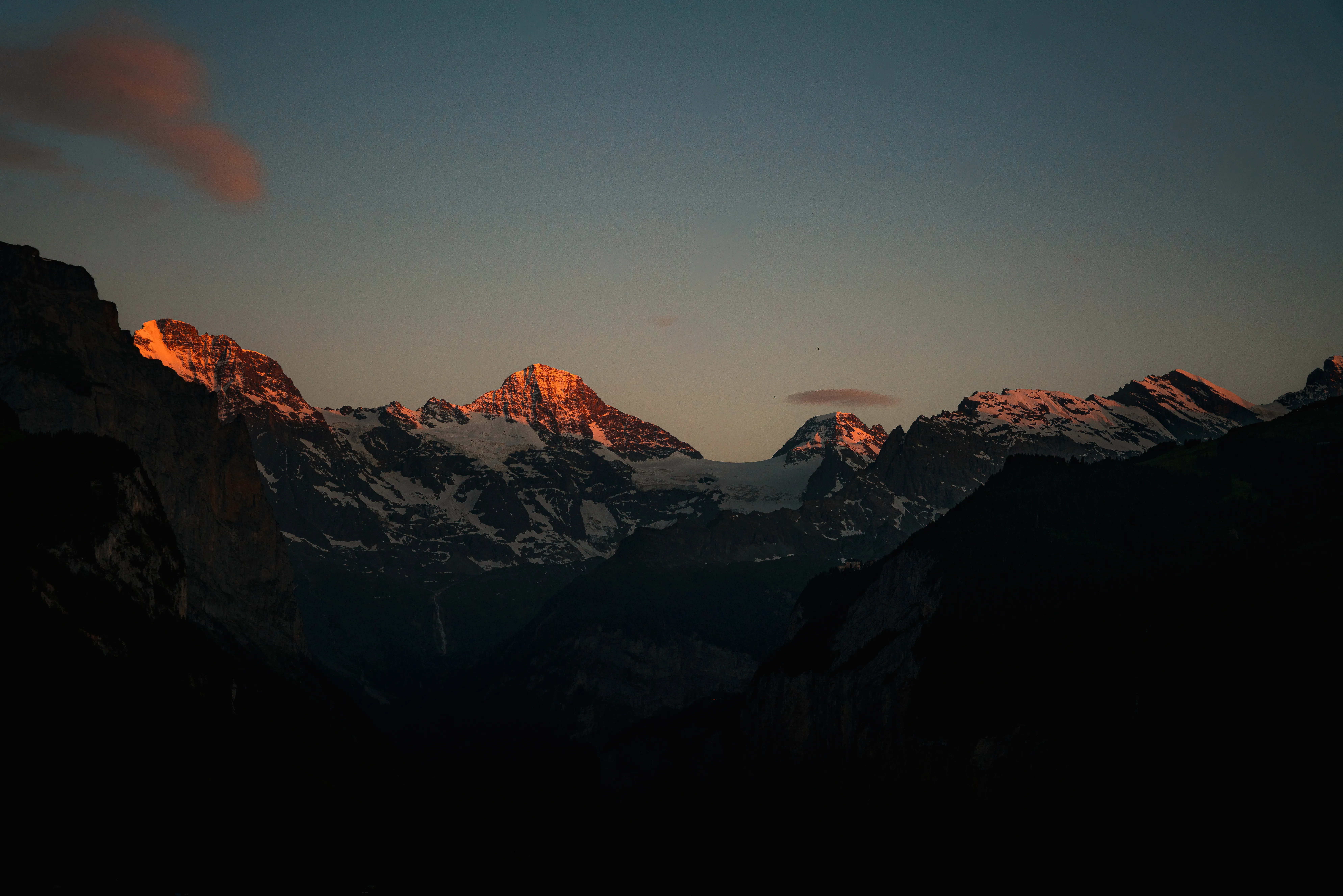 The Swiss Alps at sunset, alpenglow on snow-capped peaks above a dark valley